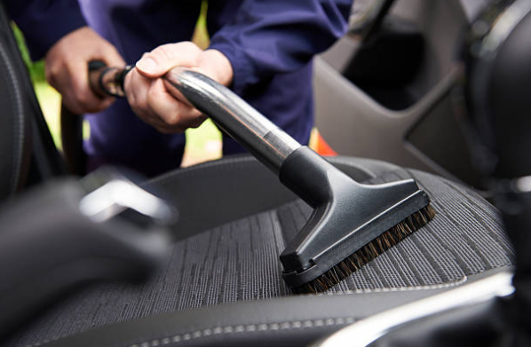 Persona aspirando asiento de auto para limpieza profunda.